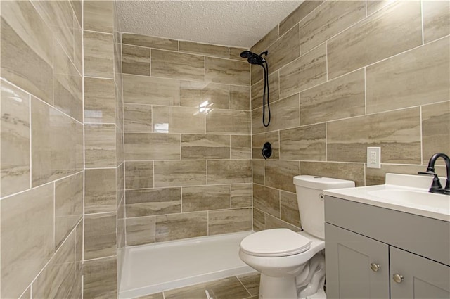 bathroom featuring vanity, toilet, tiled shower, a textured ceiling, and tile walls