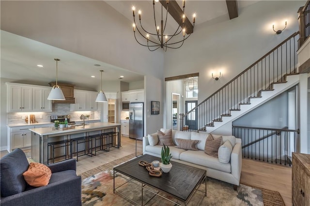 living room featuring a towering ceiling, light wood-style flooring, stairway, and beam ceiling