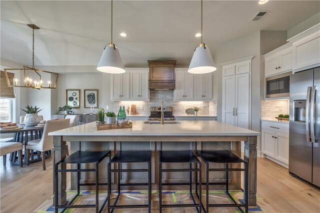 kitchen featuring a center island with sink, appliances with stainless steel finishes, white cabinets, and light countertops