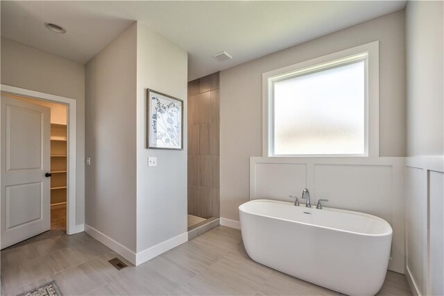 full bath featuring a freestanding tub, a spacious closet, baseboards, and a walk in shower