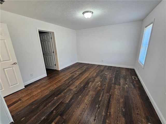 empty room with dark hardwood / wood-style floors and a textured ceiling