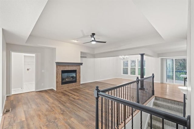 interior space featuring hardwood / wood-style floors, ceiling fan with notable chandelier, a tile fireplace, and a tray ceiling