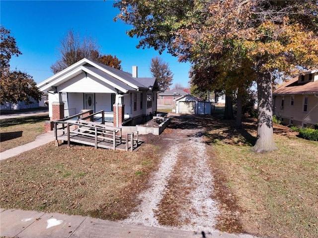 bungalow-style house with covered porch, a garage, an outdoor structure, and a front lawn