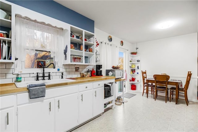 kitchen featuring white cabinets, sink, butcher block counters, and backsplash