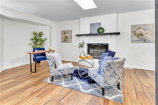 living room with a brick fireplace, a skylight, and hardwood / wood-style floors