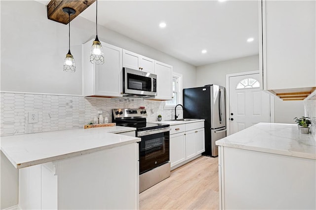 kitchen featuring light wood-type flooring, appliances with stainless steel finishes, pendant lighting, light stone countertops, and white cabinets