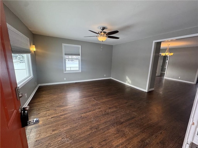 empty room featuring ceiling fan with notable chandelier and dark hardwood / wood-style floors