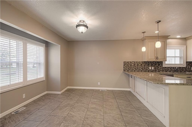 kitchen featuring light stone countertops, a textured ceiling, tasteful backsplash, decorative light fixtures, and kitchen peninsula