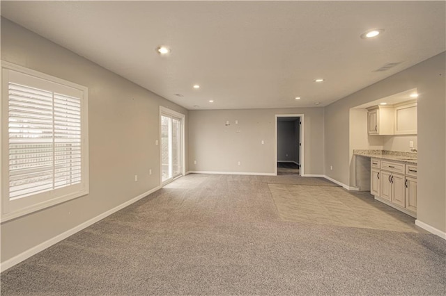 unfurnished living room featuring light carpet, a healthy amount of sunlight, and sink