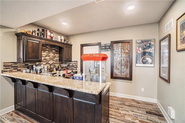 bar featuring tasteful backsplash, light stone counters, hardwood / wood-style floors, and dark brown cabinets