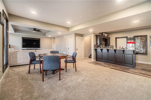 carpeted dining space with a raised ceiling, ceiling fan, and bar area