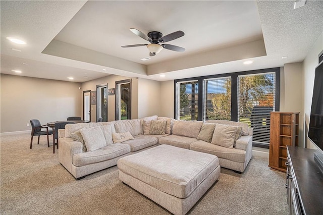 living room featuring ceiling fan, a raised ceiling, and light carpet