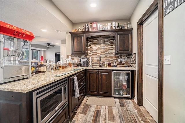 bar with sink, dark brown cabinets, stainless steel microwave, wine cooler, and tasteful backsplash