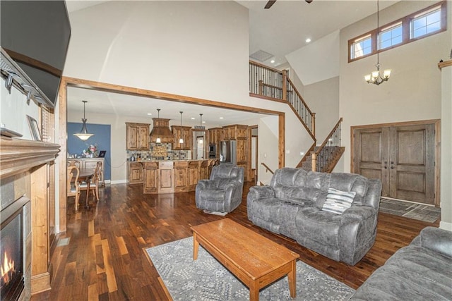 living room with a towering ceiling, a fireplace, dark hardwood / wood-style flooring, and ceiling fan with notable chandelier