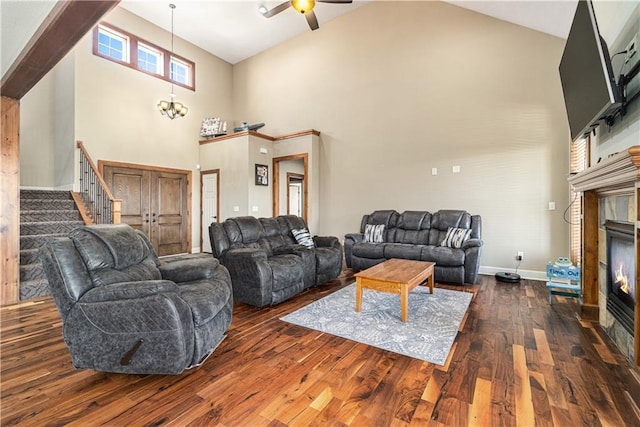 living room with dark wood-type flooring, a towering ceiling, a fireplace, and ceiling fan with notable chandelier