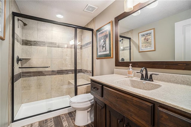 bathroom featuring vanity, toilet, a textured ceiling, and a shower with shower door