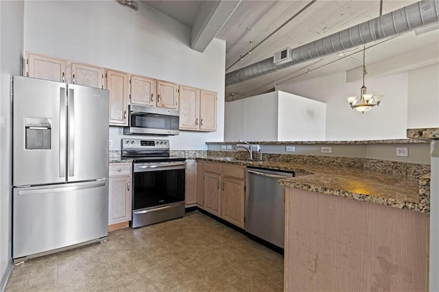 kitchen with light brown cabinetry, dark stone counters, stainless steel appliances, sink, and hanging light fixtures