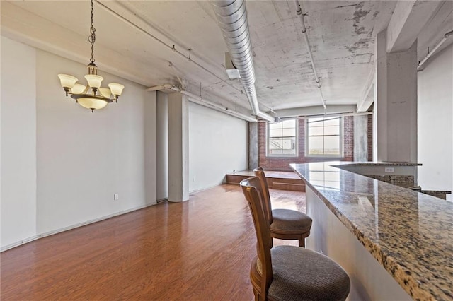 interior space featuring light stone countertops, hanging light fixtures, dark hardwood / wood-style flooring, a notable chandelier, and a breakfast bar