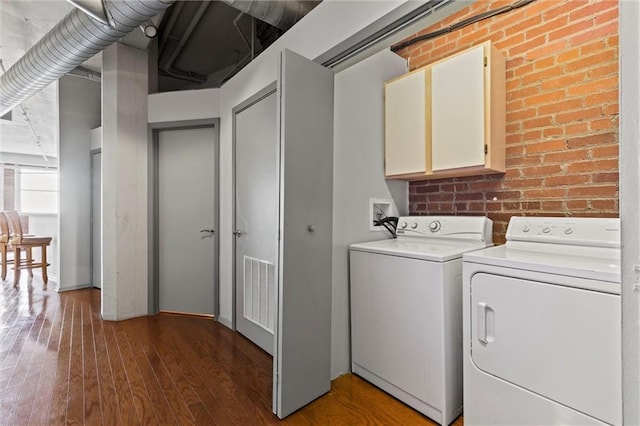 washroom featuring cabinets, dark hardwood / wood-style flooring, separate washer and dryer, and brick wall