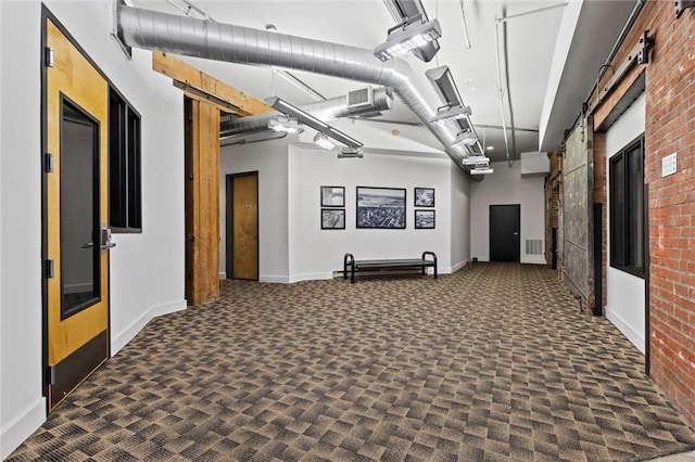 hallway featuring brick wall and dark colored carpet