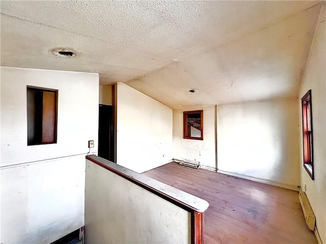 spare room featuring hardwood / wood-style flooring, lofted ceiling, a textured ceiling, and a baseboard radiator