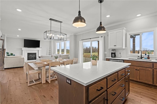 kitchen with white cabinetry, hanging light fixtures, light wood-type flooring, ornamental molding, and a kitchen island