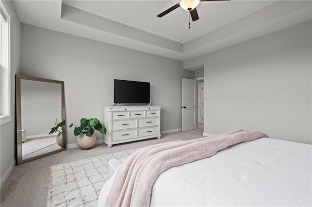 bedroom featuring a tray ceiling, light colored carpet, and ceiling fan