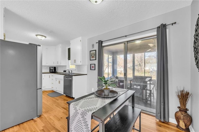 kitchen featuring a textured ceiling, stainless steel appliances, white cabinetry, and light hardwood / wood-style floors