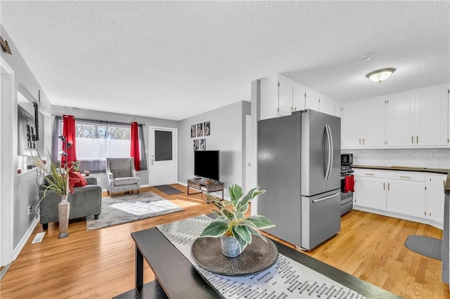 kitchen with light hardwood / wood-style floors, a textured ceiling, decorative backsplash, white cabinets, and appliances with stainless steel finishes