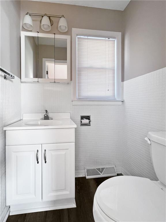 bathroom with toilet, tile walls, wood-type flooring, and vanity