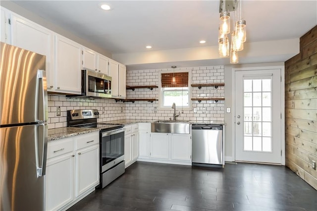 kitchen featuring pendant lighting, white cabinets, sink, wooden walls, and stainless steel appliances