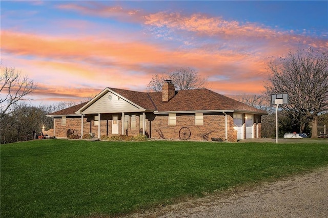 single story home with brick siding, a garage, a chimney, a lawn, and driveway