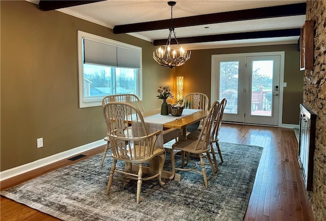 dining area featuring beam ceiling, a stone fireplace, dark hardwood / wood-style flooring, a chandelier, and ornamental molding