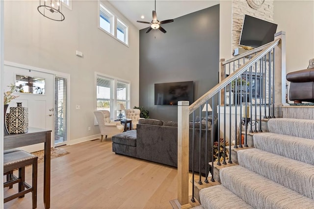 living room featuring ceiling fan with notable chandelier, a high ceiling, and light hardwood / wood-style flooring