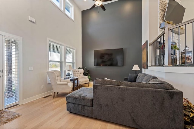 living room with light wood-type flooring, a towering ceiling, and ceiling fan