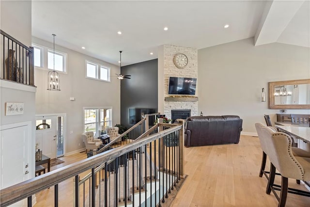 living room featuring a fireplace, high vaulted ceiling, ceiling fan with notable chandelier, and light hardwood / wood-style flooring