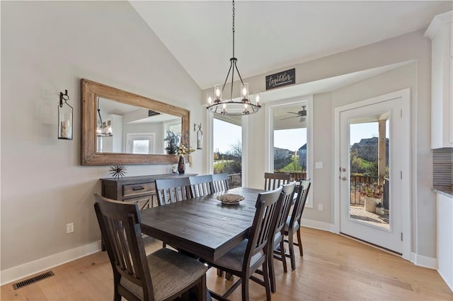 dining space with ceiling fan with notable chandelier, light hardwood / wood-style flooring, and vaulted ceiling