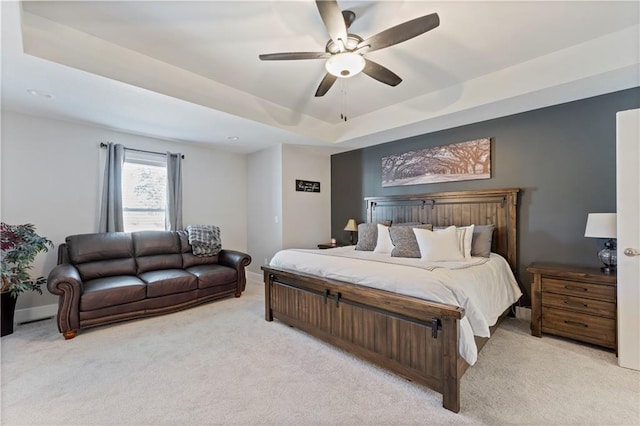 bedroom with a raised ceiling, ceiling fan, and light colored carpet