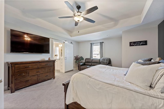 bedroom featuring light carpet, ensuite bathroom, ceiling fan, and a tray ceiling