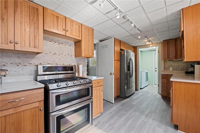 kitchen with appliances with stainless steel finishes, rail lighting, backsplash, separate washer and dryer, and light hardwood / wood-style floors