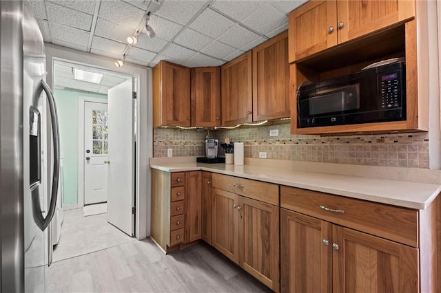 kitchen featuring stainless steel fridge, rail lighting, tasteful backsplash, black microwave, and light hardwood / wood-style floors