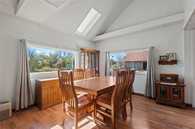 dining area featuring a skylight, light hardwood / wood-style flooring, high vaulted ceiling, and a wall mounted air conditioner