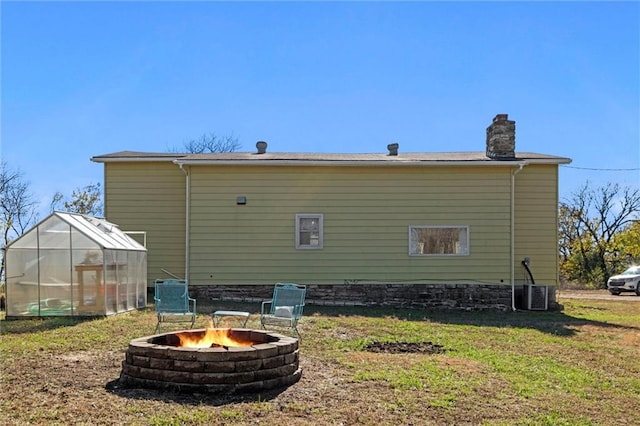 rear view of property featuring a lawn, an outbuilding, cooling unit, and an outdoor fire pit