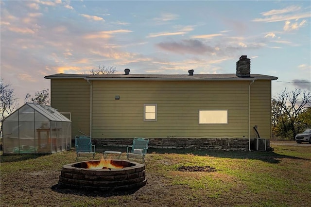 back house at dusk featuring a yard, central air condition unit, an outbuilding, and an outdoor fire pit