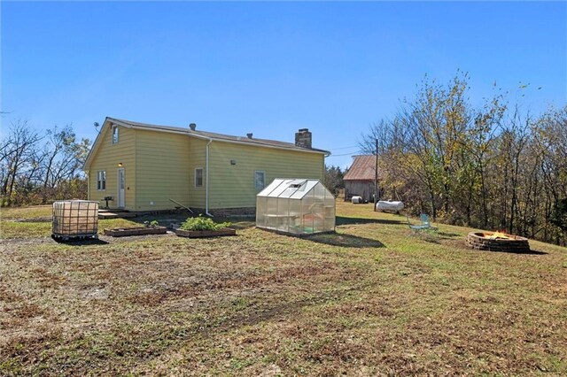 27977 W 311th St, Paola, KS 66071 - back of house featuring an exterior structure, a fire pit, a chimney, an outdoor structure, and a lawn