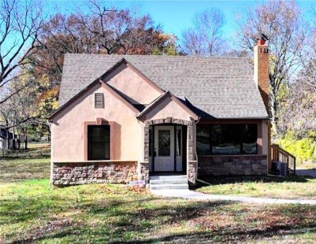 view of front facade featuring stone siding, a shingled roof, a chimney, and a front lawn