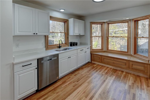 kitchen with light countertops, light wood-style flooring, stainless steel dishwasher, white cabinets, and a sink