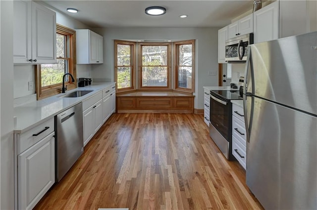 kitchen featuring appliances with stainless steel finishes, white cabinets, light countertops, and a sink