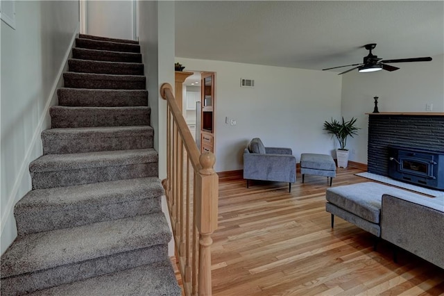 stairway with visible vents, a wood stove, ceiling fan, wood finished floors, and baseboards