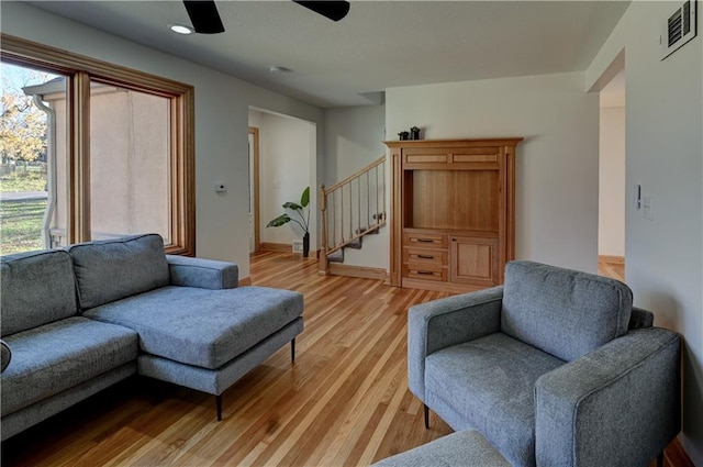 living room with ceiling fan, visible vents, baseboards, light wood-style floors, and stairway